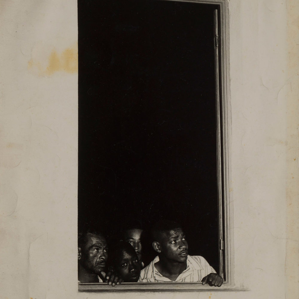 [Description: Black and white photograph of people looking out of a window] 