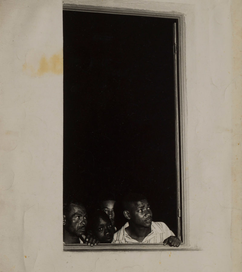 [Description: Black and white photograph of people looking out of a window] 